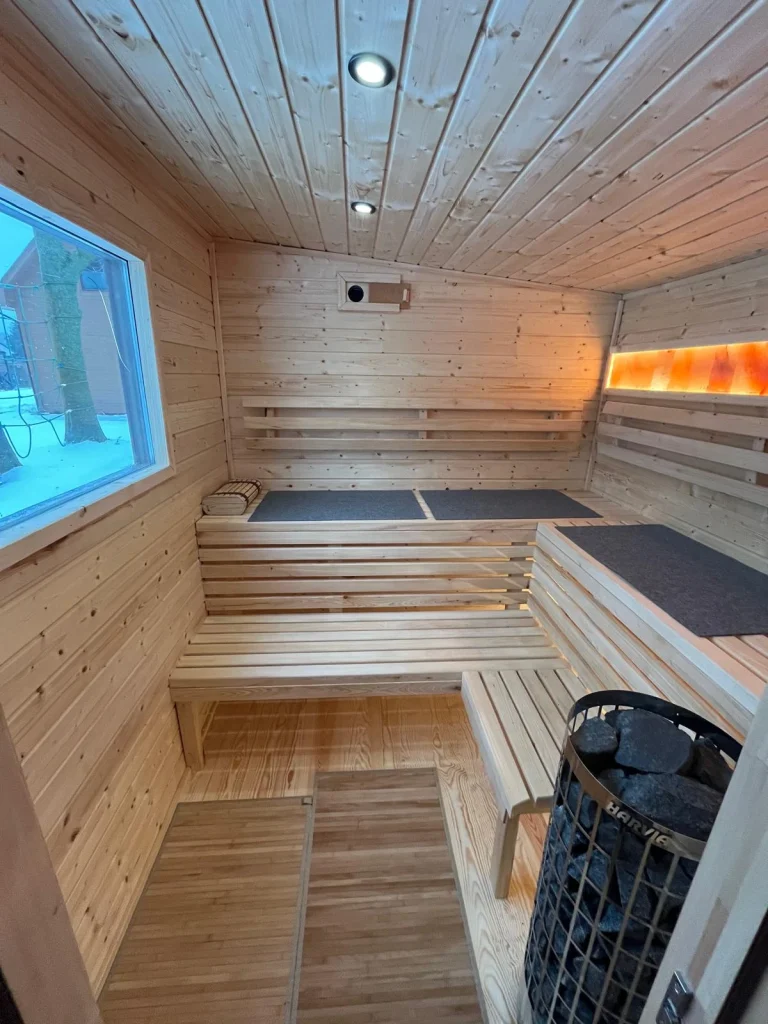 Wnętrze sauny fińskiej wykonane z jasnego drewna świerkowego z dwupoziomowymi ławami i piecem elektrycznym wypełnionym kamieniami