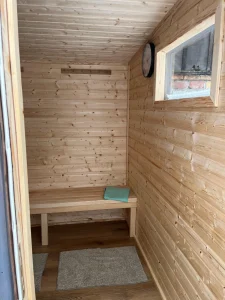 Nowoczesna kabina sauny o minimalistycznym designie, łącząca pionowe panele z jasnego drewna z elementami z hartowanego szkła.