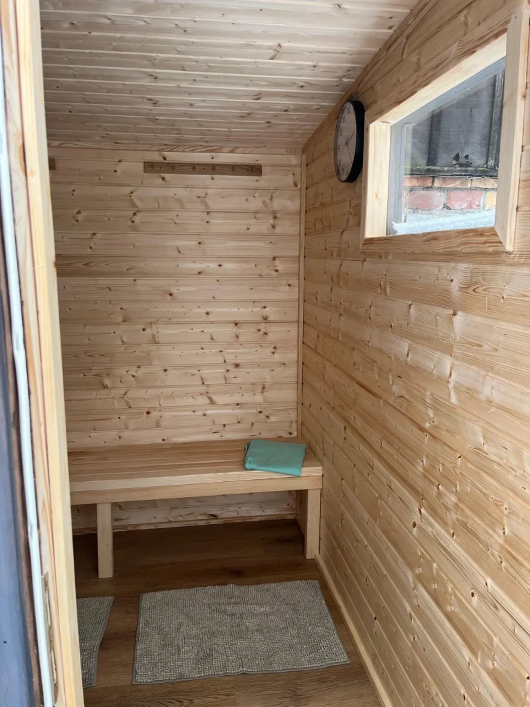 Nowoczesna kabina sauny o minimalistycznym designie, łącząca pionowe panele z jasnego drewna z elementami z hartowanego szkła.